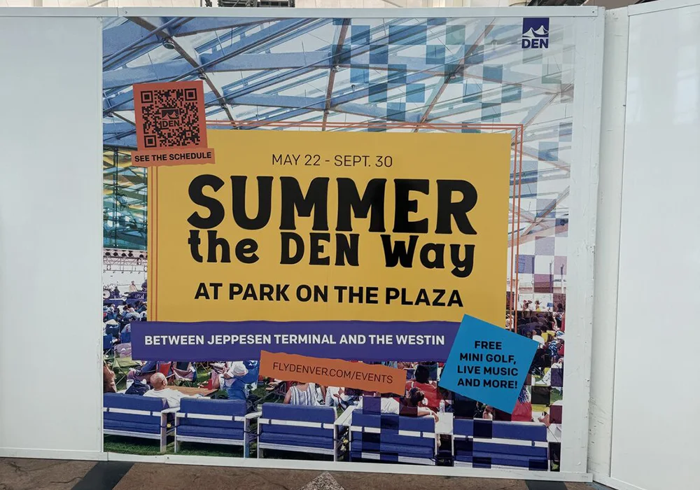 Large promotional banner at Denver International Airport advertising “Summer the DEN Way” events.
