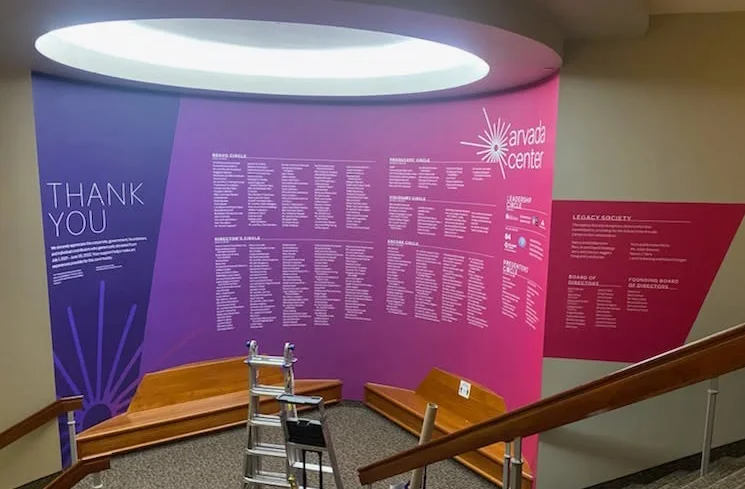Custom event display at Arvada Center featuring a large donor recognition wall with colorful graphics and supporter names along a stairway landing.