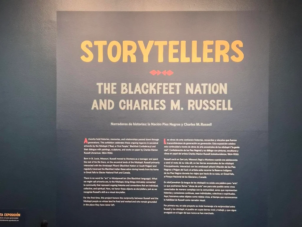 Museum wall graphic for the “Storytellers: The Blackfeet Nation and Charles M. Russell” exhibit, featuring bilingual English and Spanish text.
