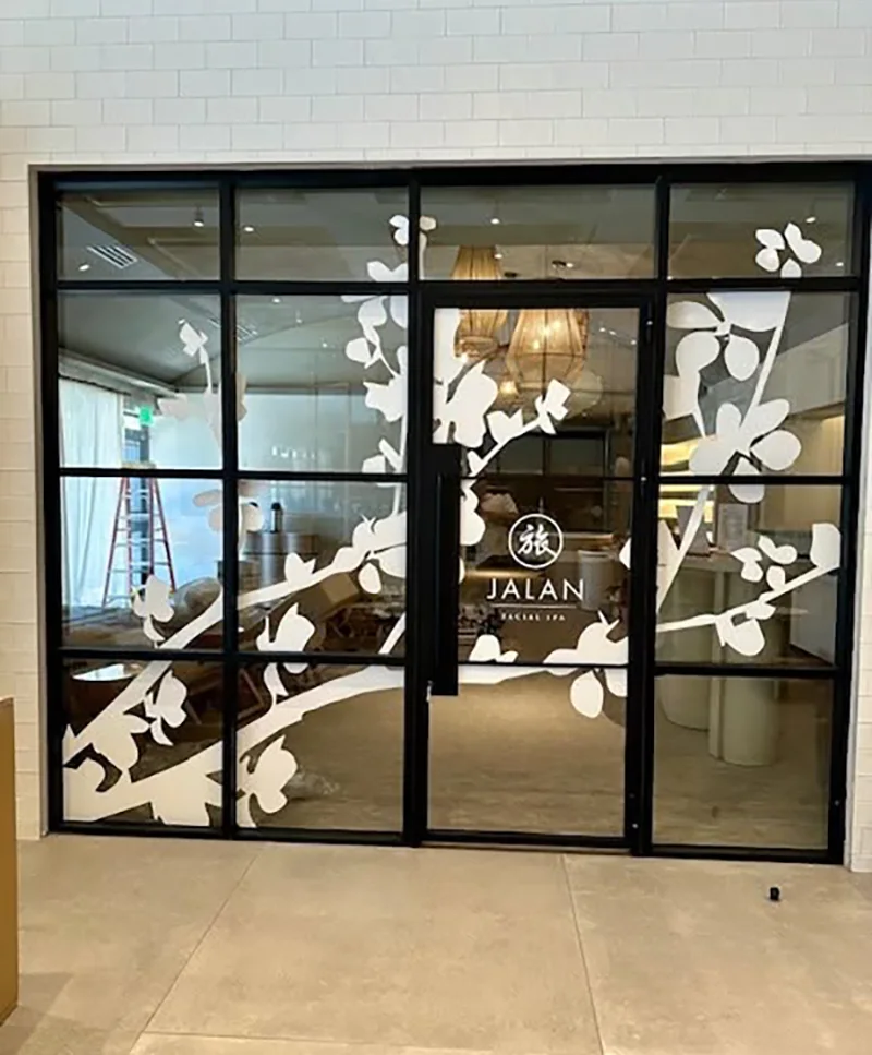 Custom window graphics featuring white floral branch designs and Jalan branding applied to black-framed glass doors and windows.